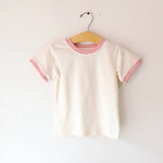 White t-shirt with pink trim on a hanger against a white background