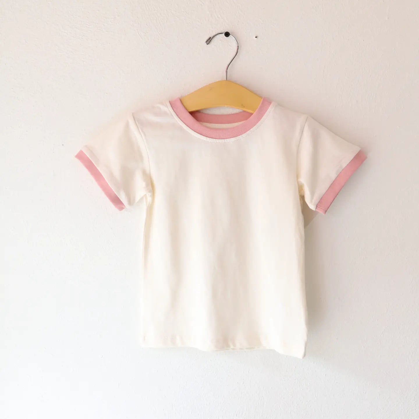 White t-shirt with pink trim on a hanger against a white background