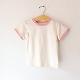 White t-shirt with pink trim on a hanger against a white background